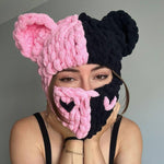 Person wearing a pink and black knitted half-mask and hat against a gray background
